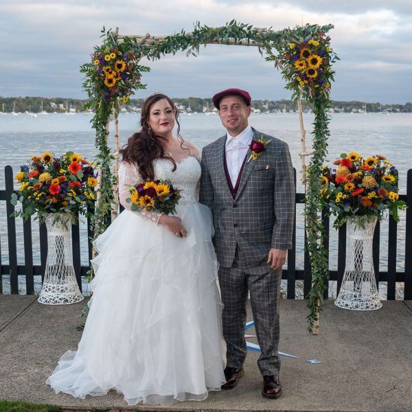 Photo of a bride and groom in front of an arch of sunflowers overlooking Salem Harbor on the grounds of The House of the Seven Gables by Gary Abramson.