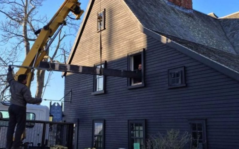 External view of a structural beam being lifted by a crane into the second floor of The House of the Seven Gables.