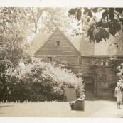 Black and white photograph of lawn and gardens with black homes in the background|Black and white photograph of a lawn with two women