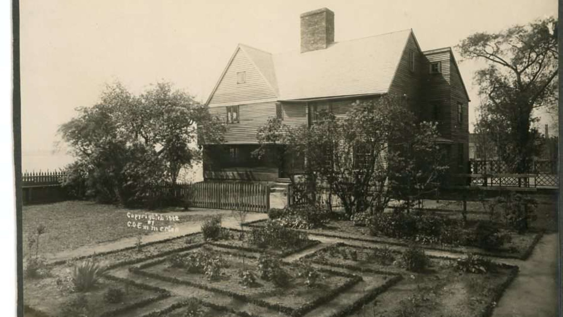A black and white photograph of a house with peaked roof and a knot-patterned garden.
