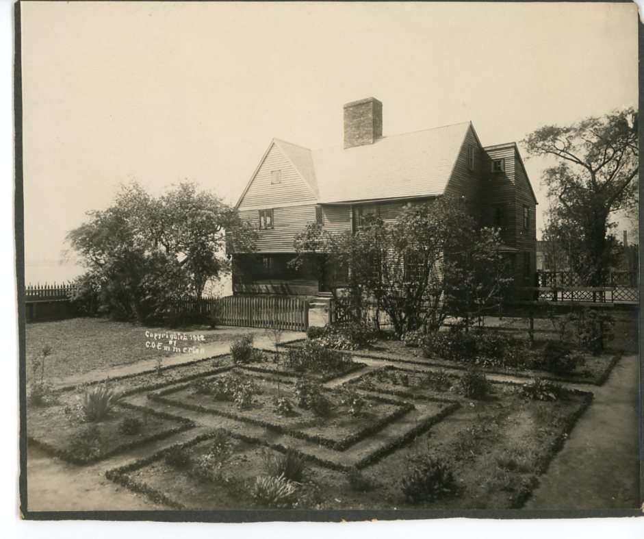 A black and white photograph of a house with peaked roof and a knot-patterned garden.