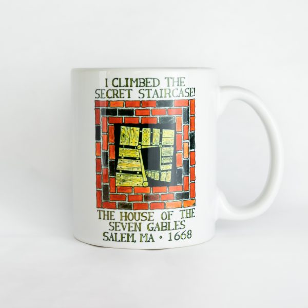 The front of the I Climbed the Secret Staircase Mug that features a drawing of the staircase going through the chimney. Written above is, "I climbed the secret staircase!" and below, "The House of the Seven Gables, Salem, MA, 1668."