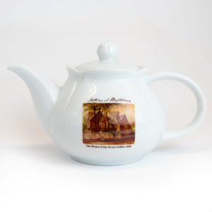 The front of the House of the Seven Gables Teapot. It is a white teapot with a rosebud knob and an image of the House of the Seven Gables going across the front.