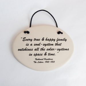 The front of the Hawthorne Quote Plaque. It is a beige ovular plaque with, "Every true & happy family is a soul-system that outshines all the solar-systems in space & time," written in black cursive lettering. It can be hung by a black cord tied to the plaque.