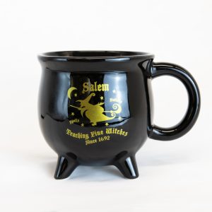 The front of the Teaching Fine Witches Since 1692 Cauldron Mug. It features the image of a witch flying across the night sky on a broom.