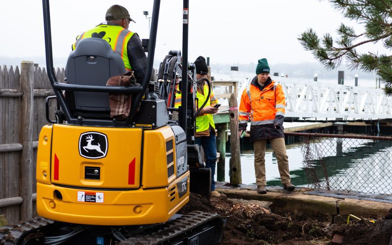 Several people in bright, reflective construction gear did test pits with a large ride-on machine.