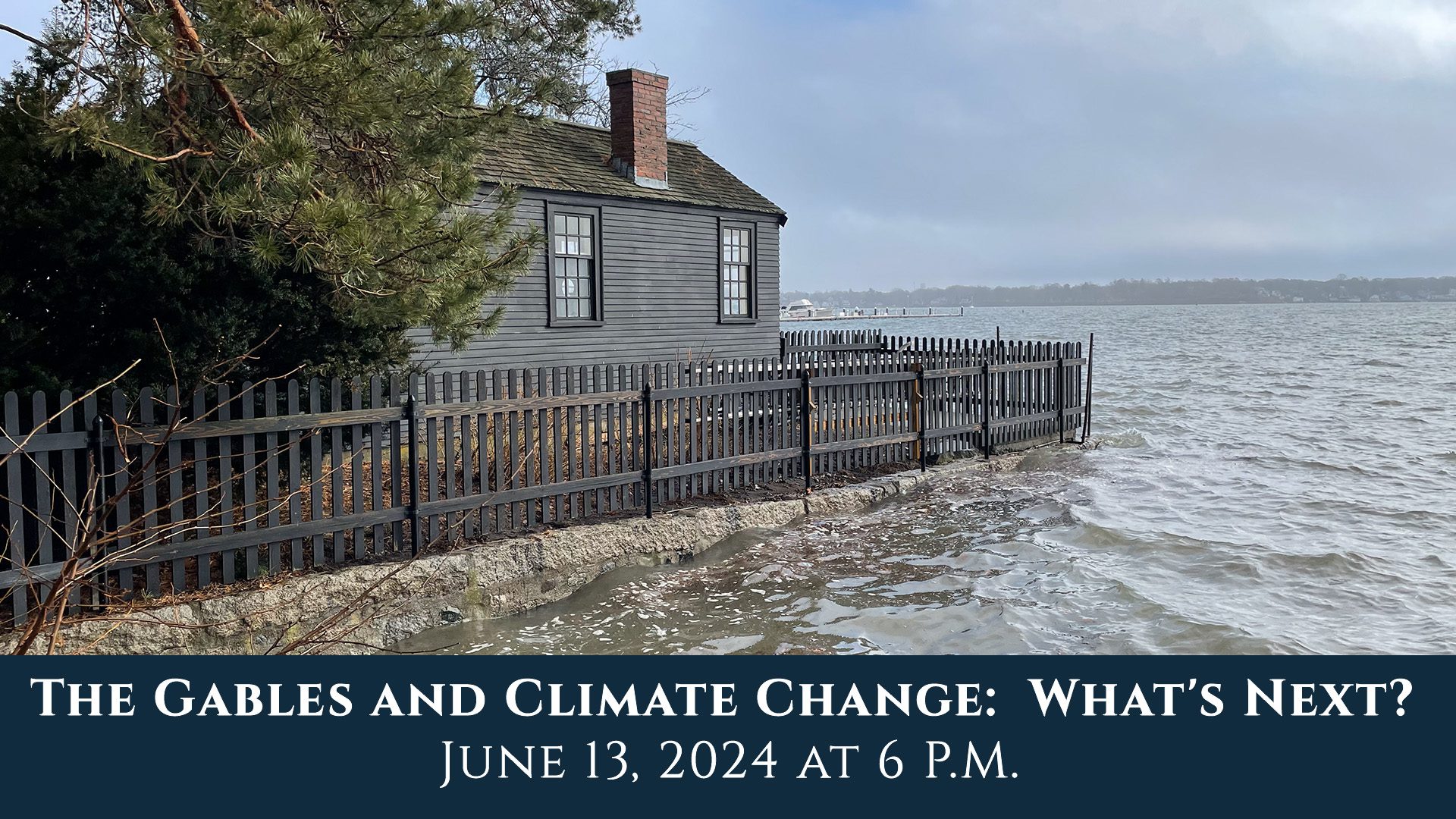 An extremely high tide in Salem Harbor meets the seaside fence outside of the Counting House with a cloudy sky in the background.