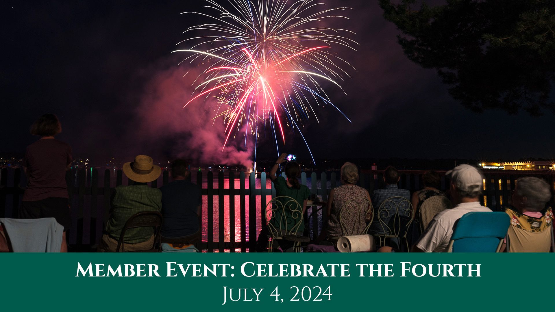 Multi-colored fireworks explode in the air over Salem Harbor as people in the foreground, facing away from the camera, watch.