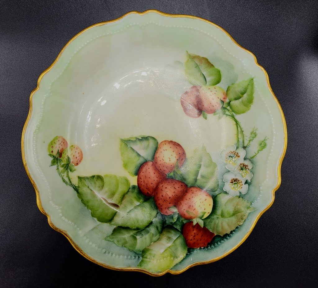 A scalloped-edge plate with hand-painted strawberries and flowers.